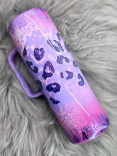 a purple cup with hearts painted on it sitting on top of a fur covered surface