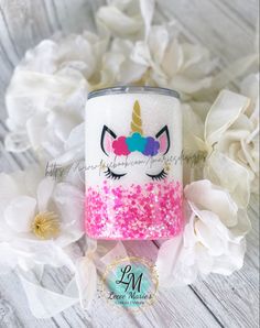 a pink and white glitter tumbler with a unicorn face on it next to flowers