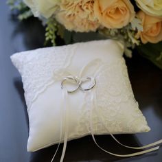 two wedding rings sitting on top of a white pillow next to flowers and a bouquet