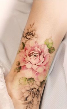 a woman's foot with a flower tattoo on her left leg and pink flowers on the right ankle