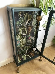 a black and green cabinet with pictures on the front, sitting next to a potted plant