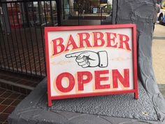 a sign that says barber open on the side of a tree trunk in front of a building