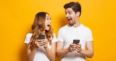 man and woman laughing while looking at their cell phones in front of each other on yellow background