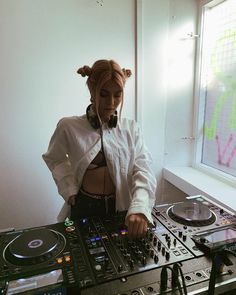 a woman with headphones on standing in front of a dj's equipment set