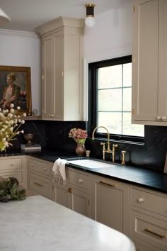 a kitchen with white cabinets and black counter tops, gold faucets and flowers on the sink