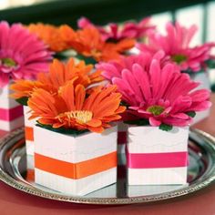 small white boxes with pink and orange flowers in them on a silver platter atop a red table cloth