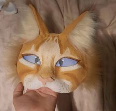 a cat mask being held up to the camera by someone's hand with blue eyes