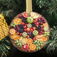 a christmas ornament made out of fruit on a wooden plate next to a tree