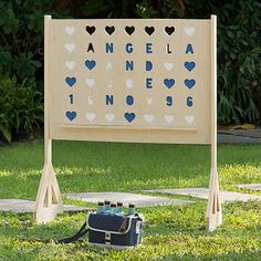 a wooden sign with hearts on it in the grass next to a bag and suitcase