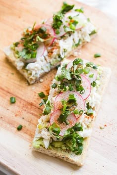 two pieces of bread on a cutting board topped with veggies and other toppings