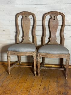 two wooden chairs sitting on top of a hard wood floor next to a white wall