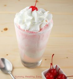 an ice cream sundae with whipped cream and cherries in a glass next to a spoon