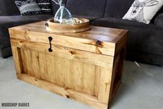 a wooden box sitting on top of a floor next to a gray couch with pillows