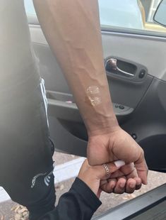 two people holding hands while standing in front of a car, one with a small tattoo on it's arm