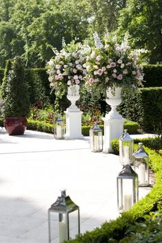 some white vases filled with flowers on top of a stone walkway in a garden