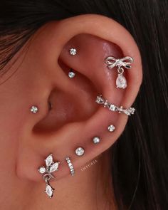 a woman with three different ear piercings on her left side, and one is wearing a bow