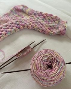 two skeins of yarn sitting next to each other with knitting needles in front of them