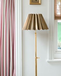 a gold floor lamp in front of a white wall with pink and blue striped curtains