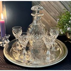 a clear glass decanter on a silver tray with wine glasses and a candle