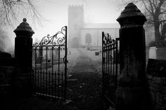 an old cemetery gate in the middle of a foggy graveyard with tombstones on either side