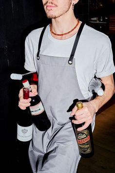 a man holding two bottles of wine in one hand and an empty bottle in the other