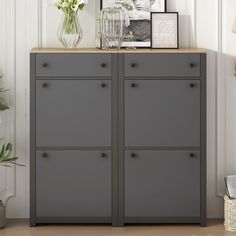 a gray cabinet with two pictures on top of it next to a potted plant