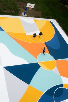 two people playing basketball on an outdoor court painted with multicolored shapes and colors