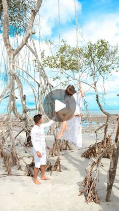 two people standing in the sand near some trees