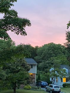 cars are parked on the side of the road near some houses and trees at sunset