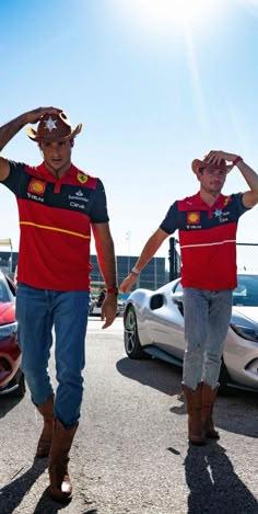 two men in red shirts and cowboy hats walk down the street with their hands on their head