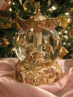 a snow globe sitting on top of a pink blanket next to a christmas tree with lights