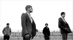 four young men are standing in front of an empty bleachers and looking off into the distance