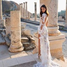 a woman standing in front of columns wearing a white dress with sheer lace on it