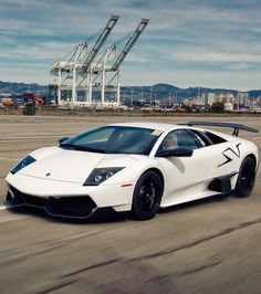 a white sports car is driving down the road in front of some cranes and buildings