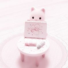 a small pink cat sitting on top of a table with a notepad and pen