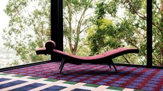 a pink chaise lounge chair sitting on top of a rug in front of a window