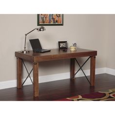 a desk with a laptop on it in front of a painting and lamp above the table