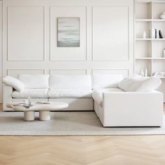 a living room with white furniture and wood flooring on one side, bookshelves in the other