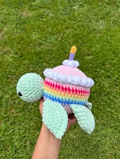 a hand holding a small crocheted toy turtle on top of green grass in the sun