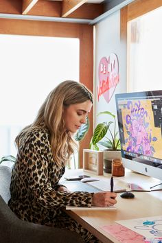 a woman sitting in front of a computer on top of a desk with a pen and paper