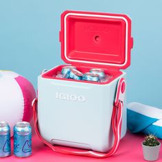 an igloo cooler with six cans of beer in it next to some beach balls