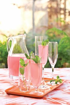 three glasses filled with pink liquid and mint sprigs sit on a wooden tray