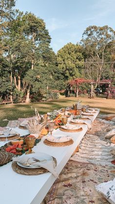 a long table is set up with plates and bowls on it in the middle of a park