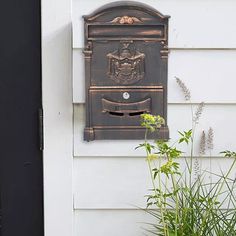 a mailbox mounted to the side of a white house next to a planter