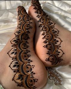 two feet covered in henna on top of a white sheet with pearls and beads