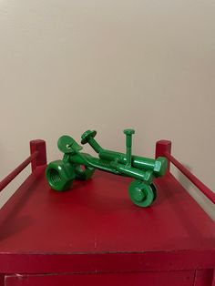 a green toy tractor sitting on top of a red table next to a white wall