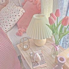 a bed with pink and white sheets, pillows and flowers in a vase on the end table