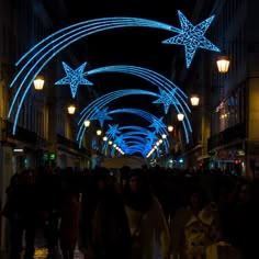 many people are walking down the street at night with lights on them and stars hanging from the ceiling