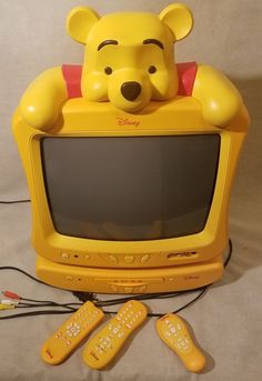 a winnie the pooh toy sitting on top of a tv set with remotes