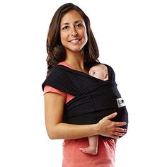 a woman holding a baby in a black wrap on her chest and smiling at the camera